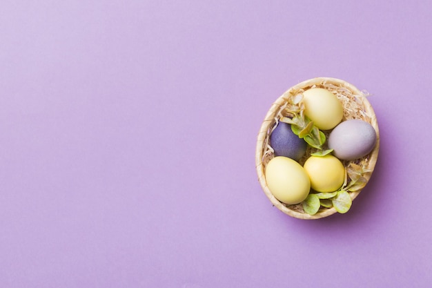 Ovos de páscoa de várias cores na cesta tecida em fundo colorido Conceito de férias de ovos de páscoa de cor pastel com espaço de cópia