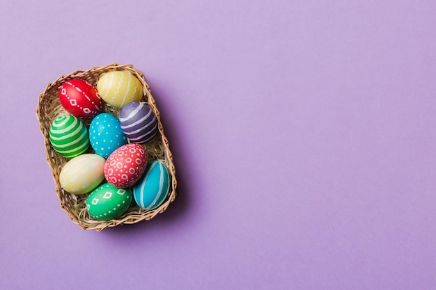 Ovos de páscoa de várias cores na cesta tecida em fundo colorido Conceito de férias de ovos de páscoa de cor pastel com espaço de cópia