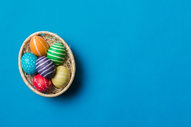 Ovos de páscoa de várias cores na cesta tecida em fundo colorido Conceito de férias de ovos de páscoa de cor pastel com espaço de cópia