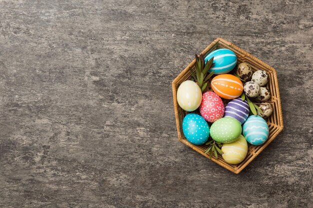 Ovos de páscoa de várias cores na cesta tecida em fundo colorido Conceito de férias de ovos de páscoa de cor pastel com espaço de cópia