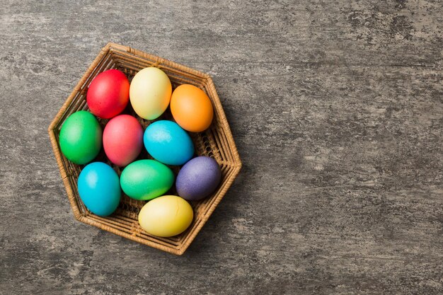 Ovos de páscoa de várias cores na cesta tecida em fundo colorido Conceito de férias de ovos de páscoa de cor pastel com espaço de cópia