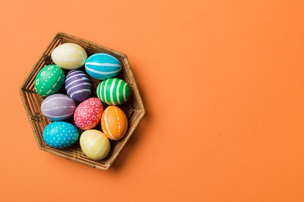 Ovos de páscoa de várias cores na cesta tecida em fundo colorido Conceito de férias de ovos de páscoa de cor pastel com espaço de cópia