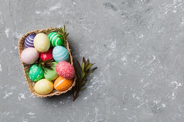 Ovos de páscoa de várias cores na cesta tecida em fundo colorido Conceito de férias de ovos de páscoa de cor pastel com espaço de cópia