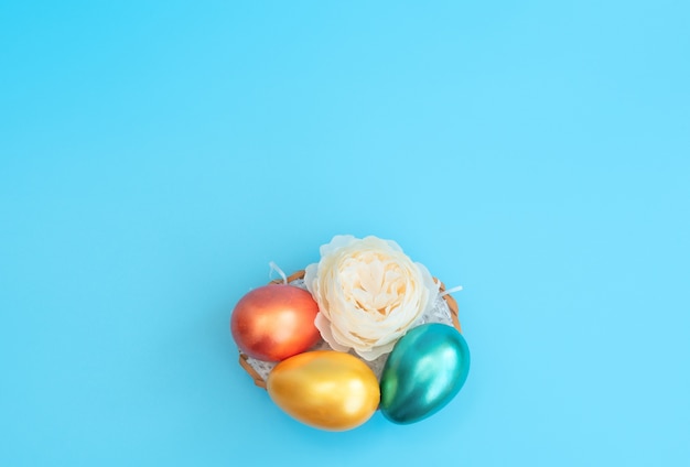 Ovos de Páscoa decorados ficam na cesta como um ninho com uma flor branca em azul
