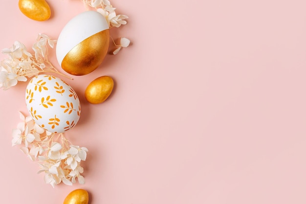 Ovos de páscoa dourados e flores brancas em fundo rosa pastel Conceito de férias Cartão de feliz páscoa com espaço de cópia