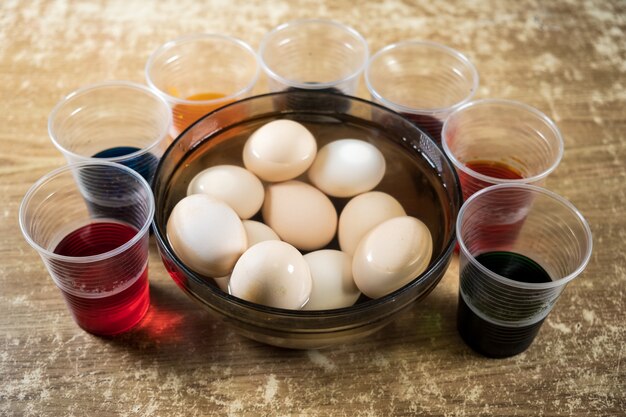 Ovos de páscoa e tintas líquidas coloridas na mesa para crianças usando tintura e pintura em ovos cozidos brancos durante a preparação para a páscoa