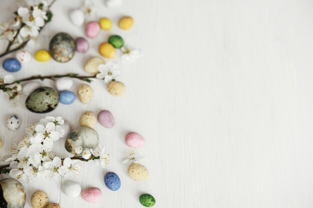 Ovos de Páscoa elegantes e flores de cerejeira em mesa branca rústica Feliz Páscoa Fronteira de Páscua com espaço para texto Mármore de corante moderno e ovos de chocolate coloridos e flores de primavera