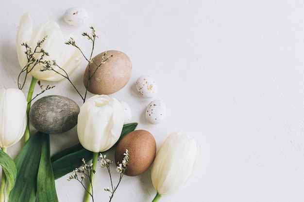 Ovos de Páscoa elegantes e fronteira de tulipas em fundo de madeira branco rústico