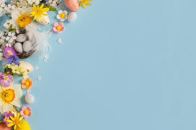 Ovos de Páscoa elegantes em flores coloridas de ninho e flores de cerejeira planas sobre fundo azul com espaço para cópia Modelo de cartão de saudação de Páscoa feliz Bandeira de férias moderna Composição festiva
