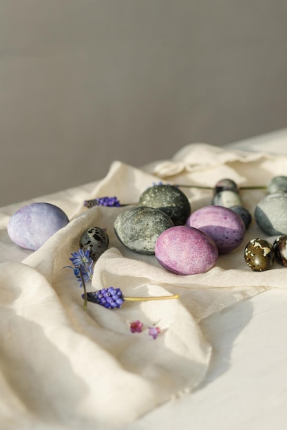 Ovos de Páscoa elegantes flores de primavera suaves e pano de linho em mesa branca rústica à luz do sol Espaço para texto Feliz Páscoa Óvulos de mármore pintado natural e roxo Saisões saudações