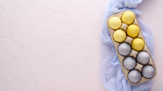 Ovos de Páscoa em tons pastéis de amarelo e azul em uma caixa de papelão em um guardanapo de pano azul em um fundo rosa com espaço de cópia