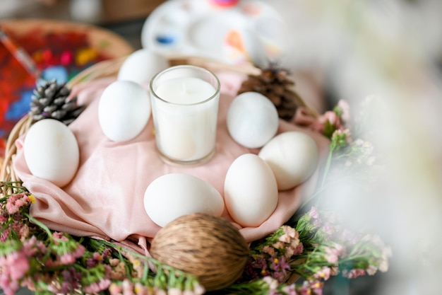 Ovos de páscoa felizes com vela branca em uma linda cesta decorada com muitas flores bonitas