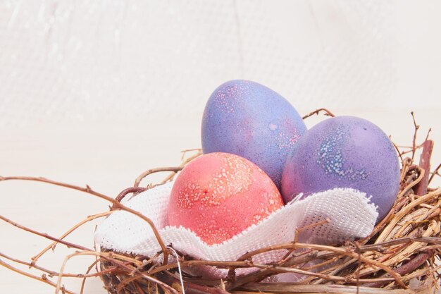 Ovos de páscoa pintados e um ninho decorativo feito de galhos em uma mesa de madeira copie o espaço