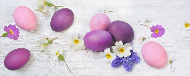 Ovos de Páscoa pintados em rosa e roxo em uma mesa entre flores e pétalas da primavera