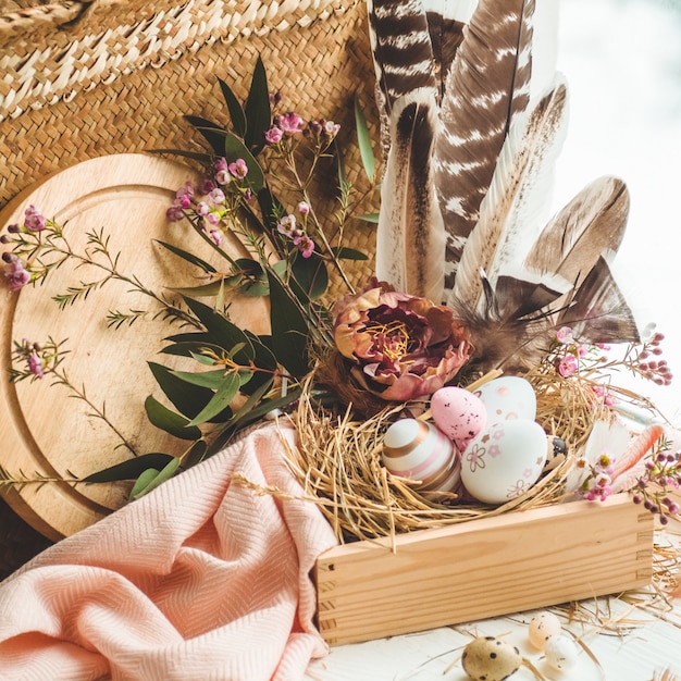 Ovos de Páscoa rosa em um ninho com decorações florais e penas perto da janela