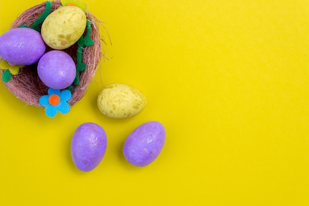 Ovos de páscoa roxos e amarelos em um ninho em um fundo amarelo vista superior