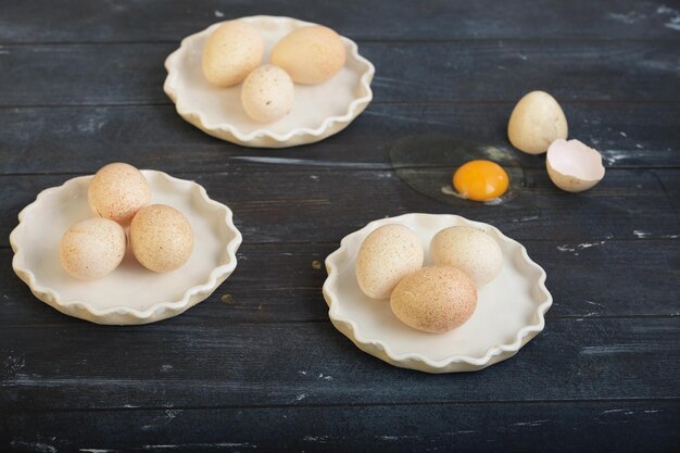 Ovos de peru em três pratos brancos e um ovo quebrado na superfície de madeira tingida áspera horizontal