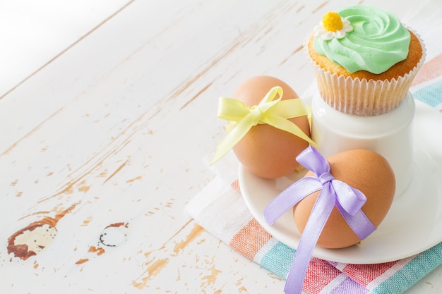 Ovos decorados com fita e cupcakes na mesa de madeira branca