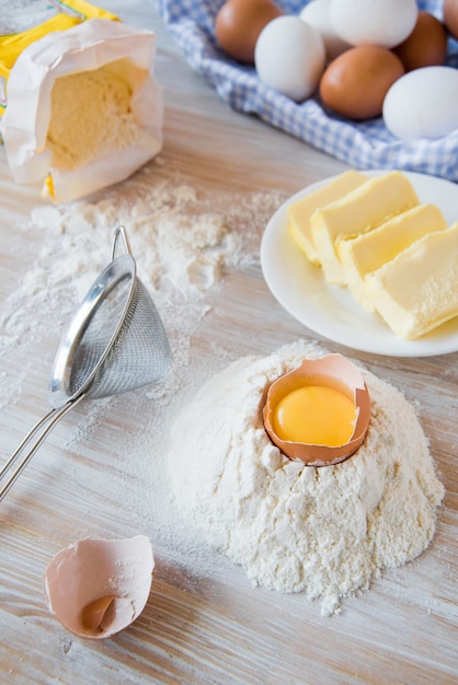 Ovos, farinha, manteiga, massa ou ingredientes de panificação em uma mesa de madeira. Foco seletivo