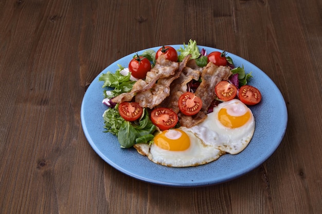 Ovos fritos com alface de bacon e tomate cereja em um prato azul em uma mesa de madeira marrom comida do país de origem