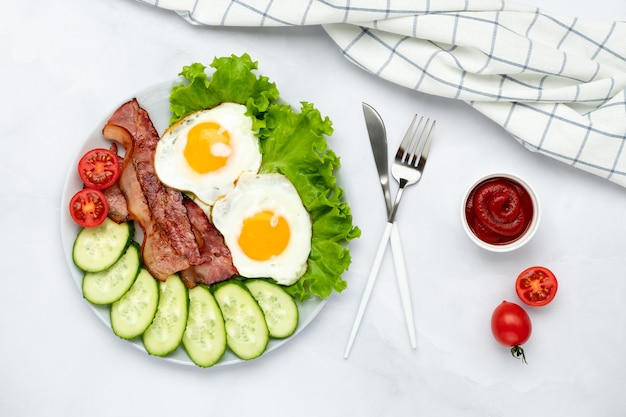 Ovos fritos com bacon e legumes em uma mesa cinza, fundo de comida de manhã. Pepinos e tomates frescos. Conceito de pequeno-almoço. Vista do topo. Composição plana lay.