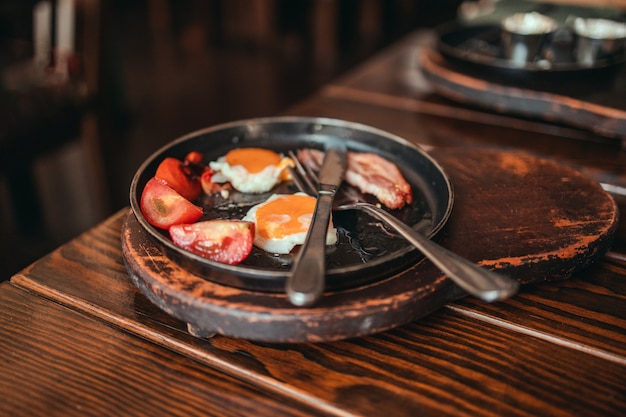 Ovos fritos com tomate bacon e torradas em um prato na mesa de madeira em um café