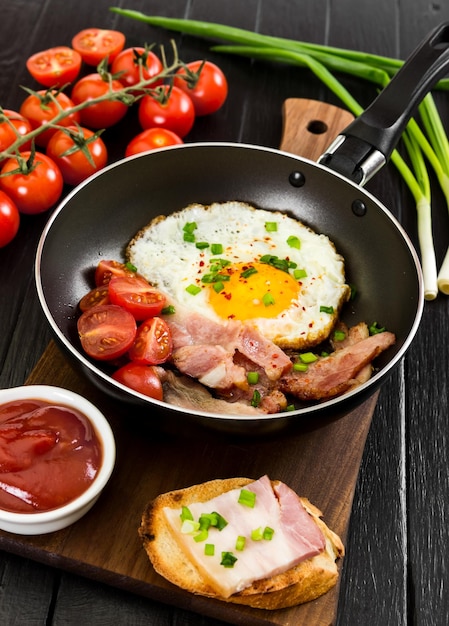 Ovos fritos com tomate cebola presunto na panela sobre fundo preto de madeira