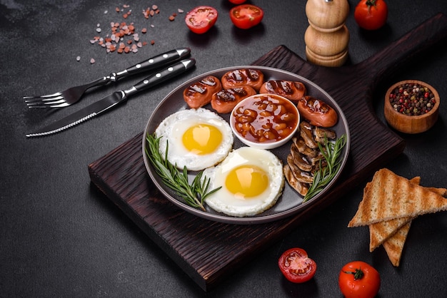 Ovos fritos de feijão de café da manhã inglês completo salsichas assadas tomates cogumelos em uma mesa de concreto escuro com pão torrado