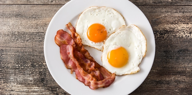 Ovos fritos e bacon no café da manhã na mesa de madeira