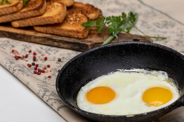 Ovos fritos em uma panela de ferro rústica, torradas em uma placa de madeira e uma xícara de café no café da manhã.