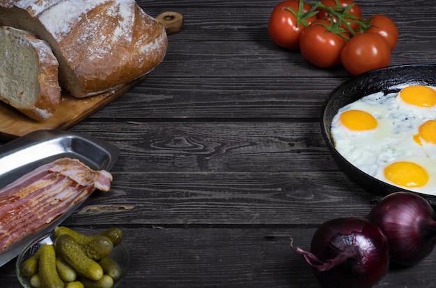 Ovos fritos rústicos em uma mesa de madeira escura com pão de cebola de tomate e pepinos em conserva em uma chave escura com espaço de cópia