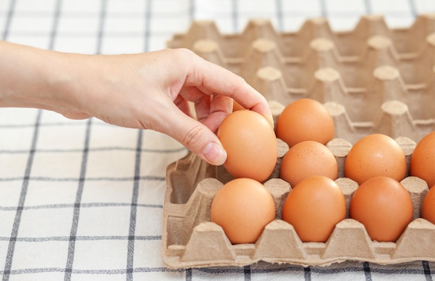 Ovos marrons de galinha estão em uma caixa de papelão comprada em uma mercearia. Café da manhã saudável. Uma bandeja para transportar e armazenar ovos frágeis. Mulher tira um ovo do pacote com a mão