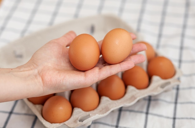 Ovos marrons de galinha estão em uma caixa de papelão comprada em uma mercearia. Café da manhã saudável. Uma bandeja para transportar e armazenar ovos frágeis. Mulher tira um ovo do pacote com a mão