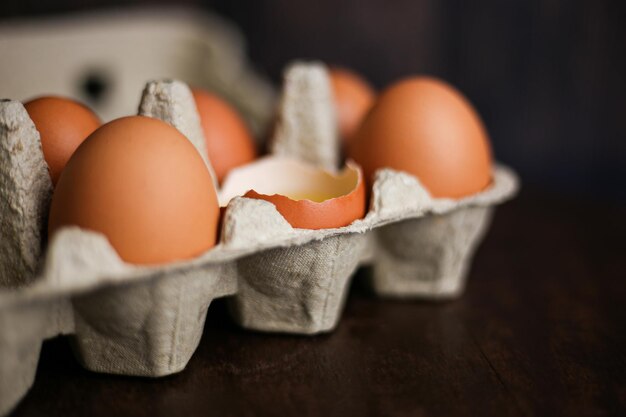 Ovos marrons frescos e um ovo quebrado com gema em uma bandeja ecológica feita de papel reciclado em madeira escura