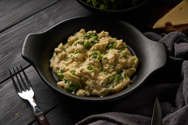 Ovos mexidos com brócolis e cebola verde servidos em prato escuro com pão na mesa preta