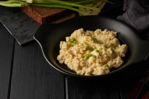 Ovos mexidos com cebola verde servidos em prato escuro com pão na mesa preta