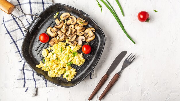 Ovos mexidos com cogumelos champignon na frigideira para café da manhã ou brunch saudável, vista de cima, copie o espaço. Ovos mexidos da receita da refeição caseira.