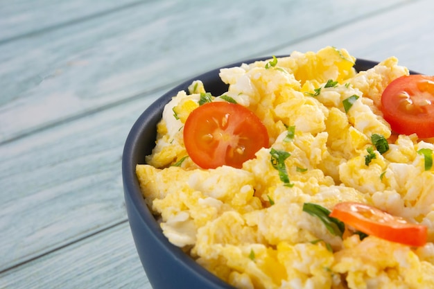 Ovos mexidos com tomate em uma tigela de mesa de madeira