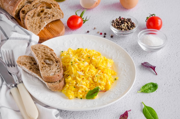 Ovos mexidos cozinhando de ovos frescos orgânicos em um prato branco com pão de centeio sobre um fundo claro com uma xícara de café. café da manhã saudável. orientação horizontal.