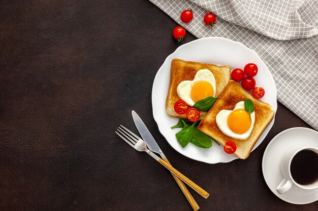 Ovos mexidos em forma de coração no prato com tomates, verduras e café
