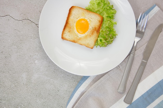 Ovos mexidos em torradas em um prato azul claro com uma alface verde em um fundo de pedra cinza com uma toalha e utensílios Café da manhã O conceito de alimentação saudável