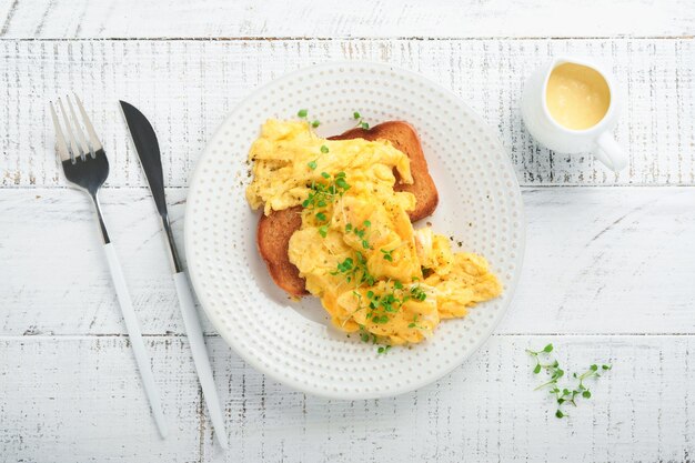 Ovos mexidos fofos e amanteigados ovos mexidos no pão com rabanete microgreen e molho holandês na chapa branca sobre fundo branco de madeira Café da manhã caseiro ou refeição de brunch Vista superior