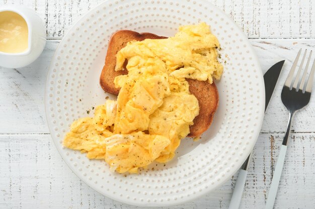 Ovos mexidos fofos e amanteigados ovos mexidos no pão com rabanete microgreen e molho holandês na chapa branca sobre fundo branco de madeira Café da manhã caseiro ou refeição de brunch Vista superior