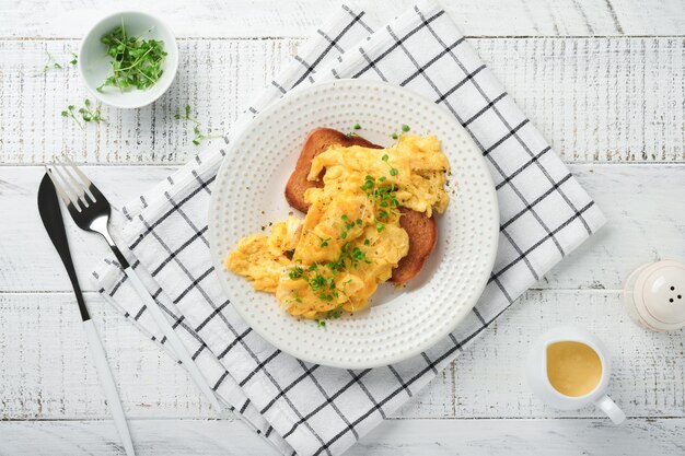 Ovos mexidos fofos e amanteigados ovos mexidos no pão com rabanete microgreen e molho holandês na chapa branca sobre fundo branco de madeira Café da manhã caseiro ou refeição de brunch Vista superior