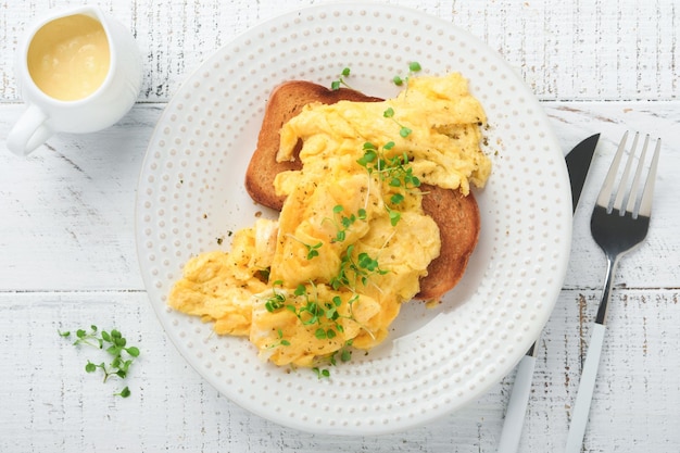 Ovos mexidos fofos e amanteigados ovos mexidos no pão com rabanete microgreen e molho holandês na chapa branca sobre fundo branco de madeira Café da manhã caseiro ou refeição de brunch Vista superior