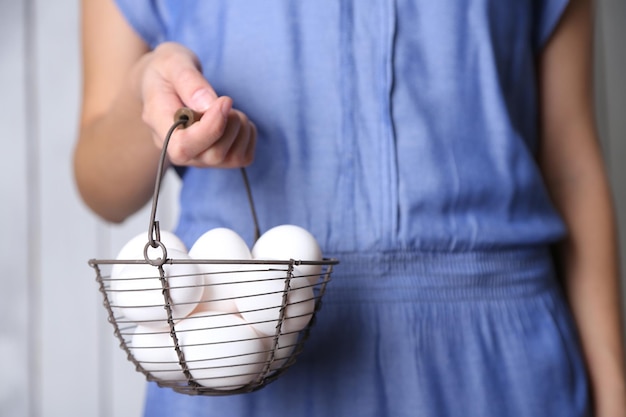 Ovos na cesta nas mãos das mulheres no fundo de madeira