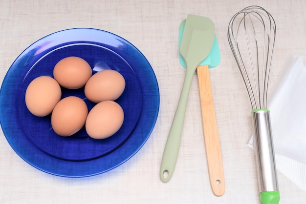 Ovos na placa azul e utensílios de cozinha estão prontos para fazer bolo caseiro Foco seletivo Processo de cozinhar em casa conceito