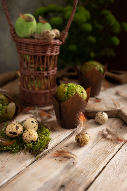 Ovos, penas e muffins com pistache na mesa de madeira clara