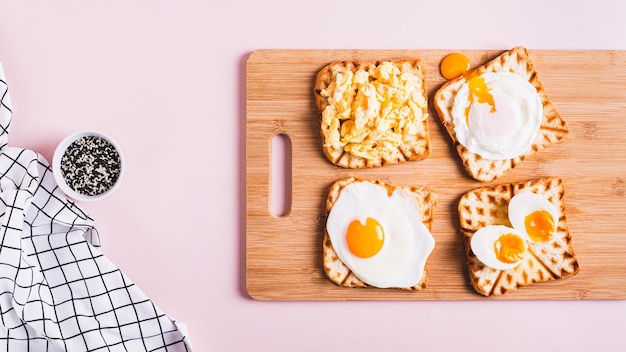 Ovos preparados de acordo com diferentes receitas em torradas em uma placa de madeira