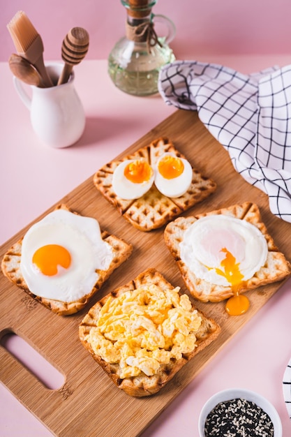 Ovos preparados de acordo com diferentes receitas em torradas em uma tábua de madeira, vista vertical